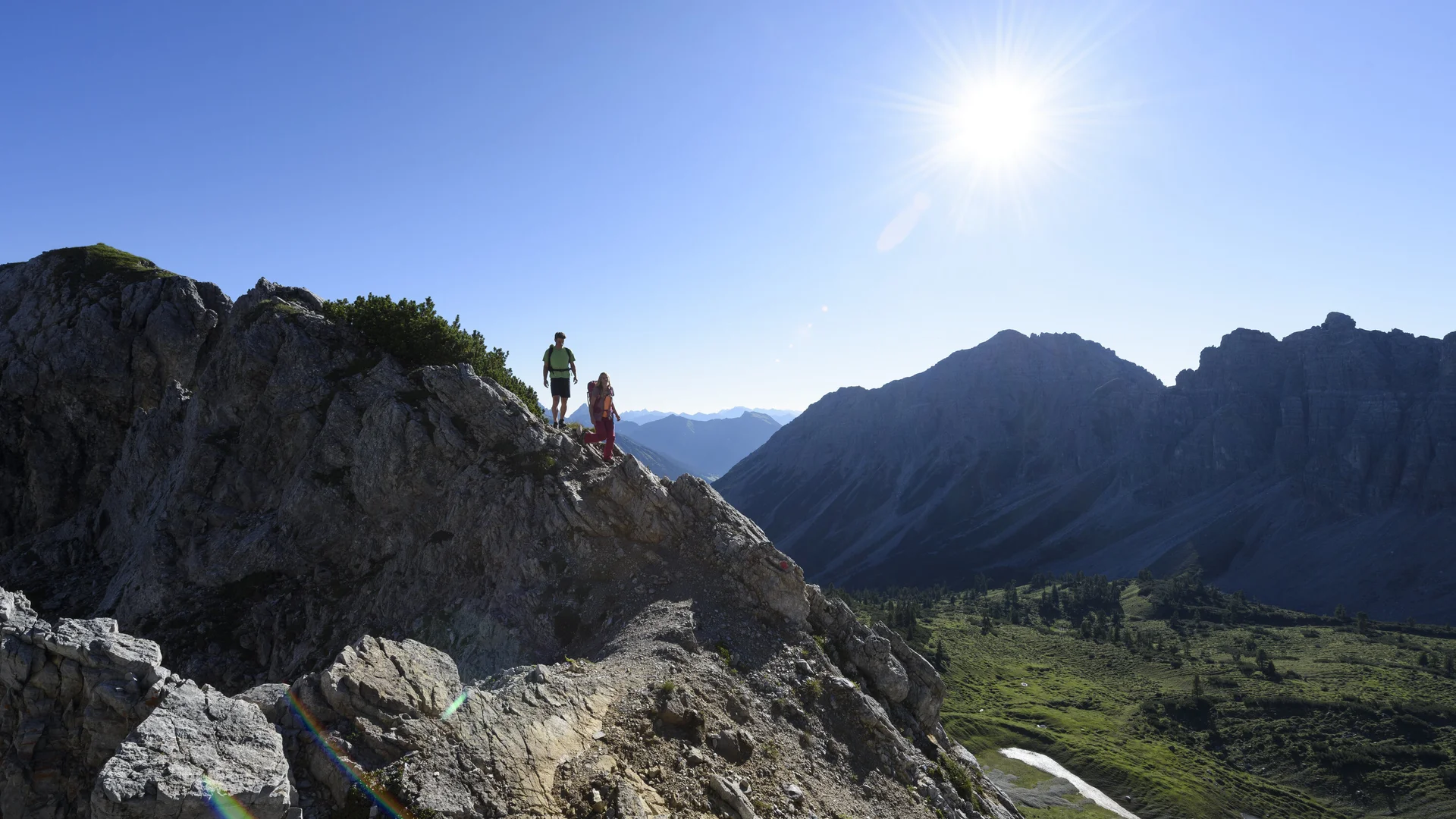 Zwei Wanderer auf einem Felsgrat. Im Hintergrund grüne Bergwiesen | © DAV / Wolfgang Ehn