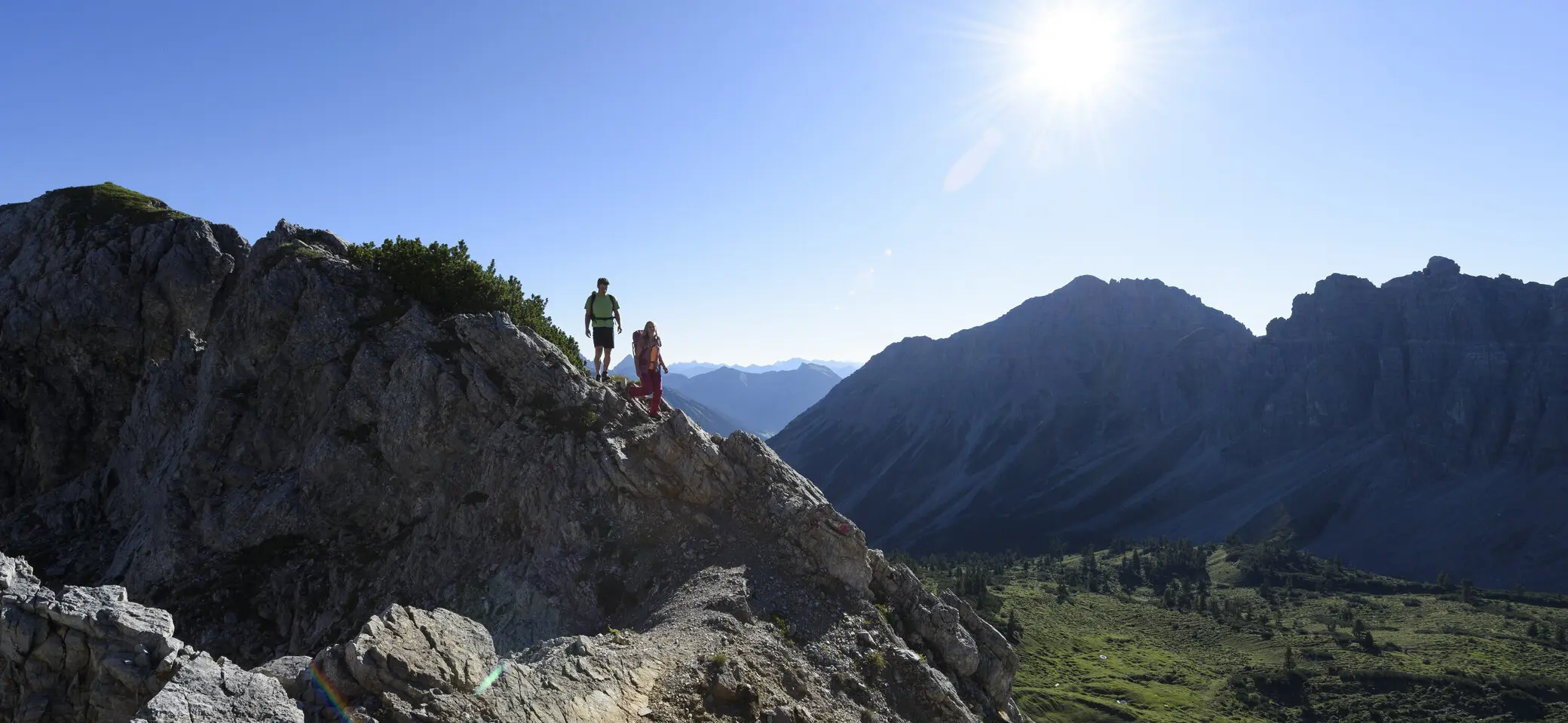 Zwei Wanderer auf einem Felsgrat. Im Hintergrund grüne Bergwiesen | © DAV / Wolfgang Ehn